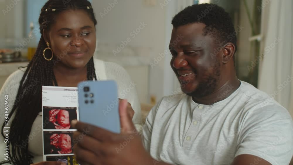 Handheld shot of young black spouses calling parents on video on smartphone to show ultrasound image of unborn baby Handheld shot of young black spouses calling parents on video on smartphone to show ultrasound image of unborn baby