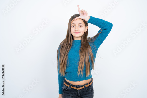 Young beautiful teen girl wearing blue T-shirt  making fun of people with fingers on forehead doing loser gesture mocking and insulting. © Jihan