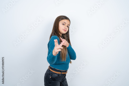 Joyful Young beautiful teen girl wearing blue T-shirt wink and points index fingers at camera, chooses someone, makes finger gun pistol.