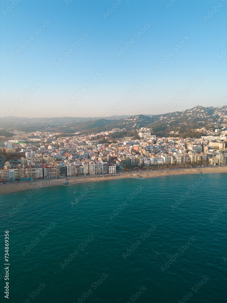 Aerial view of Lloret del Mar City. Mediterranean coastal town in Catalonia, Spain. One of the most popular Costa Brava beaches. Famous travel destination. Vertical photo. Sunset warm colours