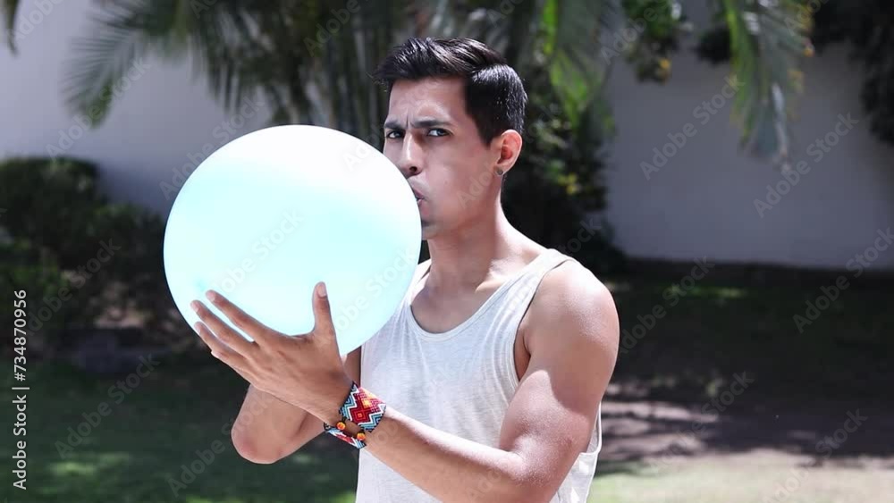 Latino man blowing up balloon in street at day time. Slow motion