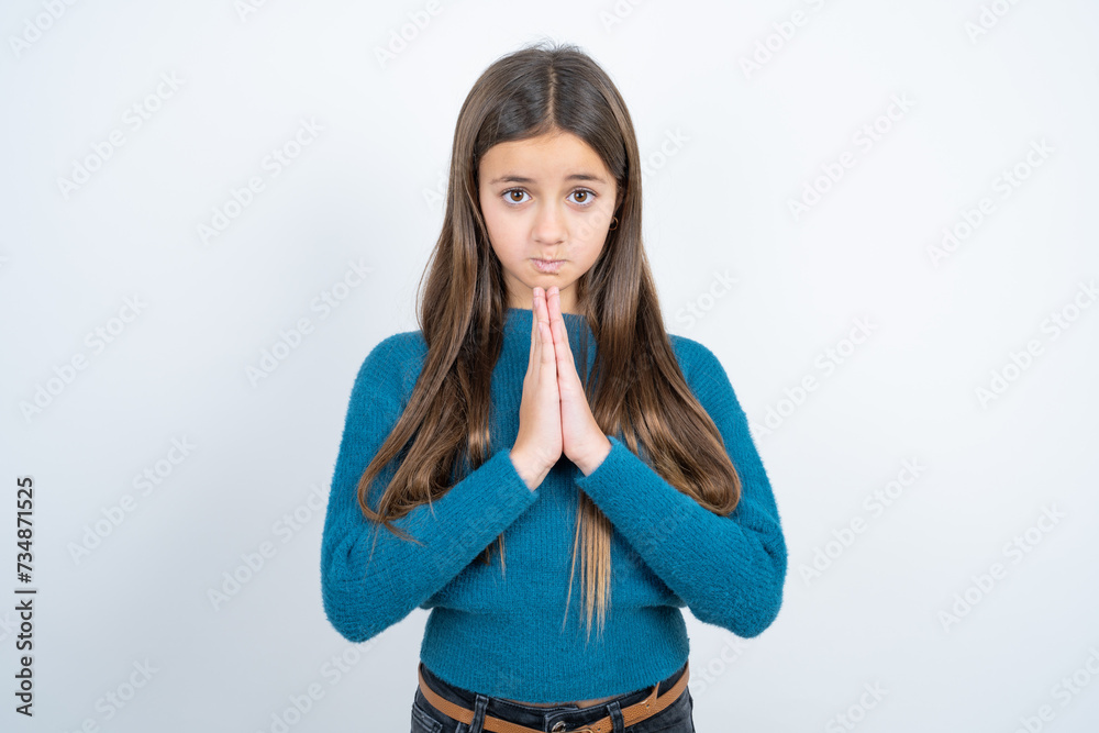 Positive Young beautiful teen girl wearing blue T-shirt smiles happily, glad to receive pleasant news from interlocutor, keeps palms together, People emotions concept.