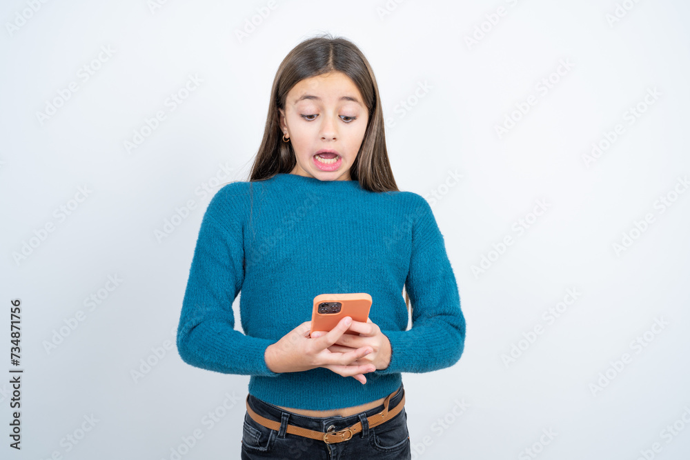 Surprised Young beautiful teen girl wearing blue T-shirt using smartphone reading social media news, or important e-mail