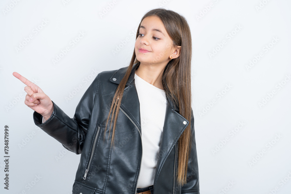 Young beautiful teen girl wearing biker jacket points to side on blank space demonstrates advertisement. People and promotion concept Young beautiful teen girl wearing biker jacket points to side on blank space demonstrates advertisement. People and promotion concept