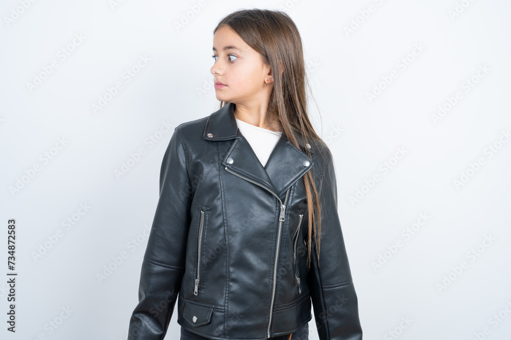 Young beautiful teen girl wearing biker jacket stares aside with wondered expression has speechless expression. Embarrassed model looks in surprise Young beautiful teen girl wearing biker jacket stares aside with wondered expression has speechless expression. Embarrassed model looks in surprise