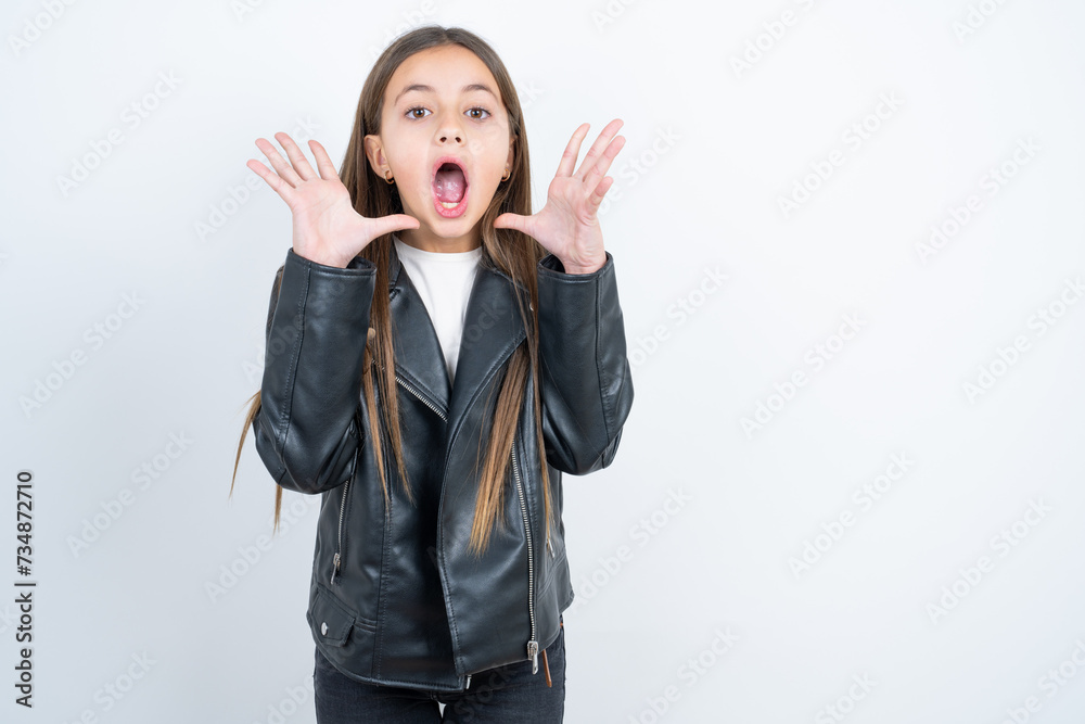 Surprised happy Young beautiful teen girl wearing biker jacket, glad to see big discounts on clothes, expresses shock, keeps hands near head, jaw dropped. Surprised happy Young beautiful teen girl wearing biker jacket, glad to see big discounts on clothes, expresses shock, keeps hands near head, jaw dropped.