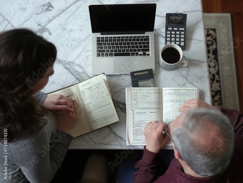 A couple discussing their monthly expenses and budgeting goals at the kitchen table with notebooks and calculators © CG Design