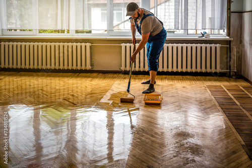 Professional worker lacquering old parquet floors using roller. Floor renovation