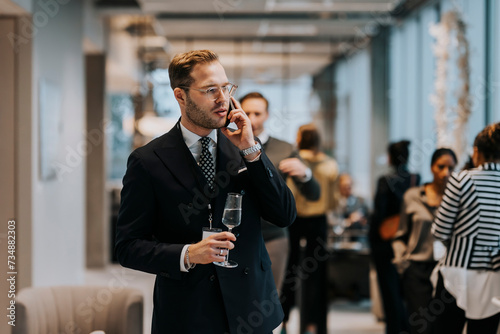 Young businessman holding champagne flute while talking on mobile phone during business conference