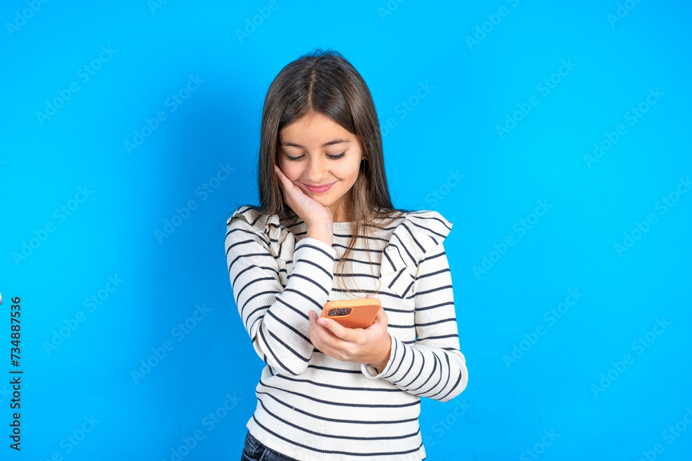 Beautiful kid girl wearing striped T-shirt holding in hands cell reading sms using new app 5g Beautiful kid girl wearing striped T-shirt holding in hands cell reading sms using new app 5g