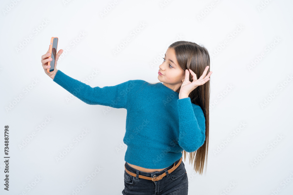 beautiful kid girl wearing blue sweater smiling and taking a selfie ready to post it on her social media. beautiful kid girl wearing blue sweater smiling and taking a selfie ready to post it on her social media.