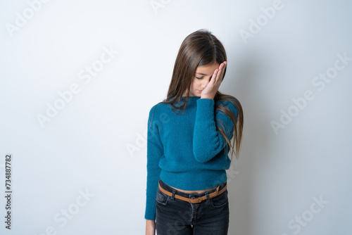 Tired overworked beautiful kid girl wearing blue sweater has sleepy expression, gloomy look, covers face with hand, has eyes shut, gasps from tiredness, fatigue after party
