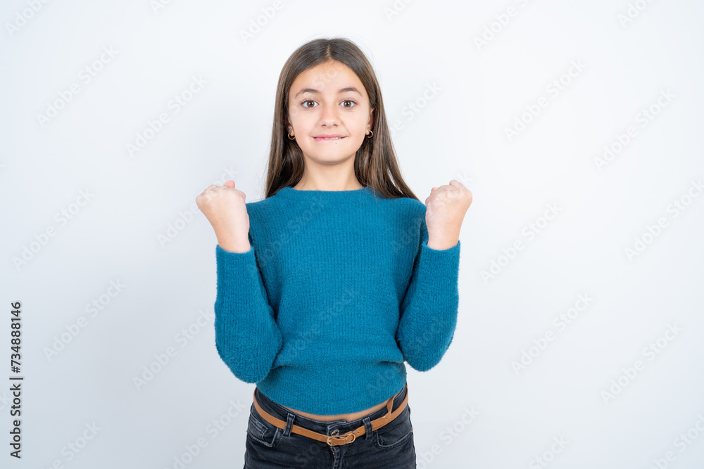 beautiful kid girl wearing blue sweater celebrating surprised and amazed for success with arms raised and open eyes. Winner concept. beautiful kid girl wearing blue sweater celebrating surprised and amazed for success with arms raised and open eyes. Winner concept.
