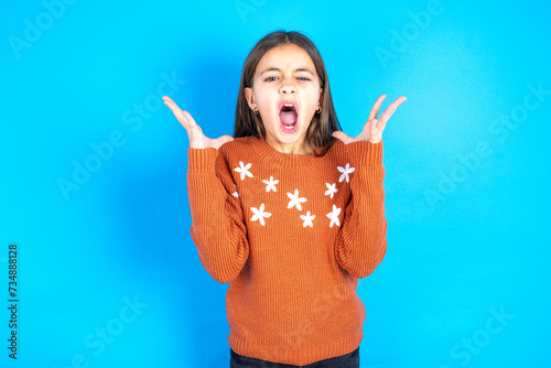 Crazy outraged beautiful kid girl wearing orange sweater screams loudly and gestures angrily yells furiously. Negative human emotions feelings concept