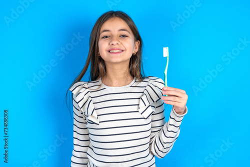 beautiful kid girl wearing  striped T-shirt holding a toothbrush and smiling. Dental healthcare concept.
