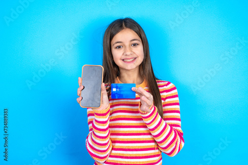 Photo of adorable Young kid girl wearing striped t-shirt holding credit card and Smartphone. Reserved for online purchases