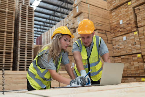 Male and female warehouse worker working with laptop computer in lumber storage warehouse. Workers working in timber storage warehouse. Manufacturing and warehouse concept