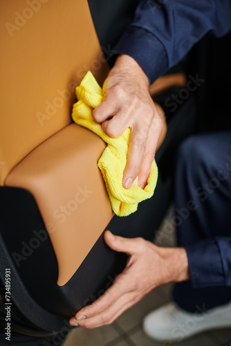 cropped view of dedicated professional serviceman in comfy uniform cleaning car with yellow rag