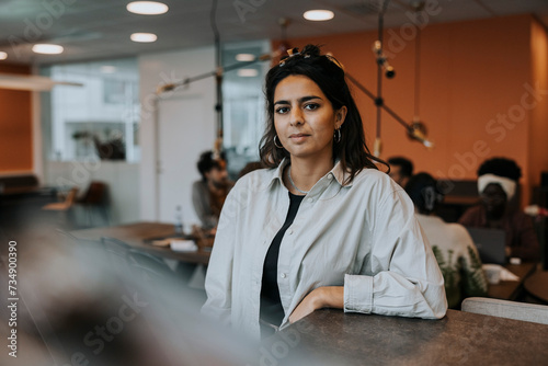 Portrait of confident young businesswoman standing by desk in office
