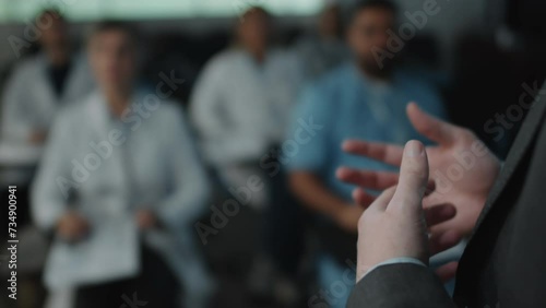 Close up foreground focus shot of unrecognizable man standing in front of audience in conference hall and gesticulating while giving speech photo