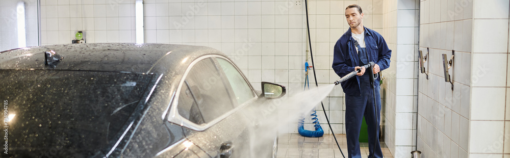 good looking devoted worker in blue uniform with collected hair using hose to wash black car, banner good looking devoted worker in blue uniform with collected hair using hose to wash black car, banner