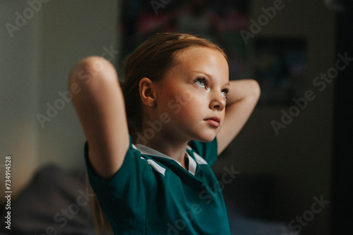 Contemplative girl with hands behind head looking away at home photo