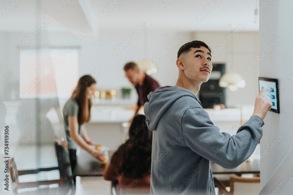 Teenage boy adjusting lights of room through digital tablet mounted on wall by family Teenage boy adjusting lights of room through digital tablet mounted on wall by family