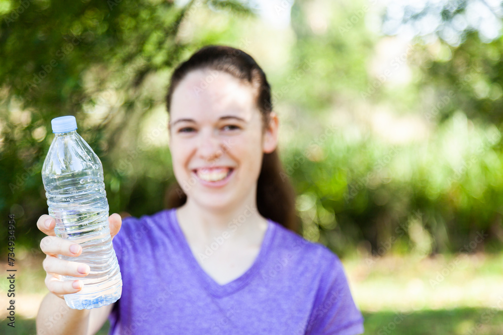 Young woman in purple holding out plastic waterbottle with clean water in it Young woman in purple holding out plastic waterbottle with clean water in it