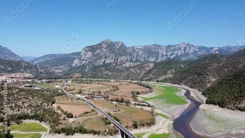 Toma aérea grabada con un dron sobrevolando una vía por donde circulan coches y un río. Hay algunas montañas al fondo en el horizonte. photo