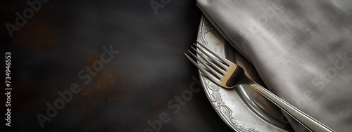 A silver fork and plate with a gray napkin on a black background, offering plenty of space for text. This elegant and minimalist image exudes sophistication and class