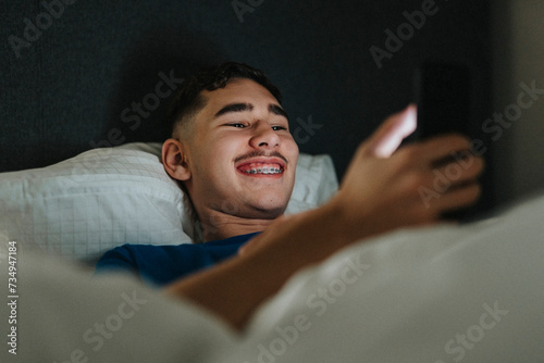 Smiling teenage boy using smart phone while lying in bedroom at home photo