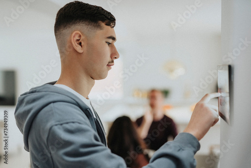 Side view of boy using home automation app through digital tablet mounted on wall photo