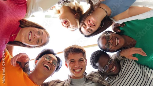 Low angle view of a group of multiracial friends standing on a circle, smiling and embracing together. Young teenagets laughing and looking at camera. Team of confident people on a coaching meeting photo