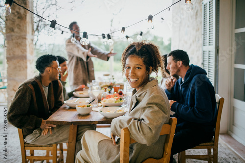 Portrait of happy young woman sitting at dining table with friends during dinner party photo