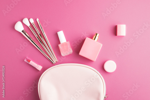 Top view of pink cosmetic bag with assorted makeup products and accessories on bright pink background. Nail polish, perfume, lipstick, cream and make-up brushes. photo