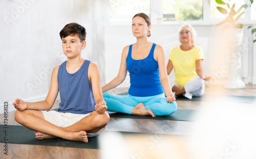 Son, mother and grandmother sitting on floor doing yoga exercise lord of fishes pose