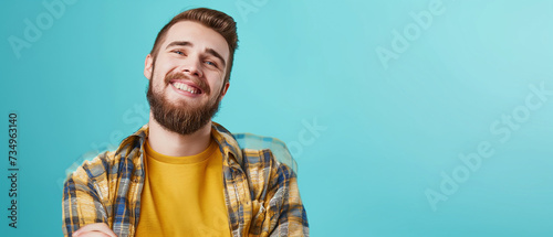 Retrato de um jovem sorridente com barba e uma camisa amarela sobre um fundo azul