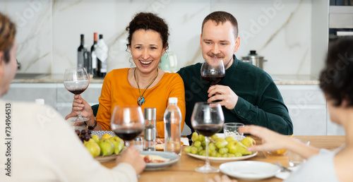 Couple are sitting at table with friends, drinking wine and enjoying snacks, chatting merrily, raise glass to, celebrating important event.