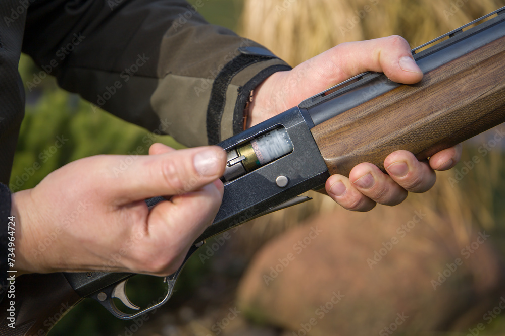 A close-up view of a hunter's hand loading a cartridge into a hunting rifle.