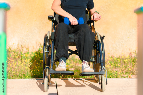 Anonymous woman seated in a wheelchair holding blue dumbbells on her lap, ready for an upper body workout session photo