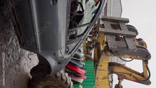 Forklift stacks cars into pile in junk yard close up with fork tidying up scrap vehicles. a Bulldozer moves a broken car through a landfill in rainy weather, Vertical view. slow motion photo