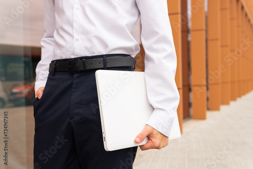 Close-up of a professional anonymous man in a white shirt and navy pants holding a laptop, ready for a productive business day photo