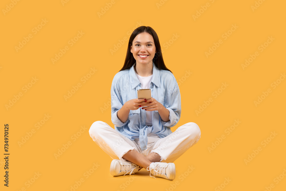 Happy european woman sitting with phone on yellow background Happy european woman sitting with phone on yellow background
