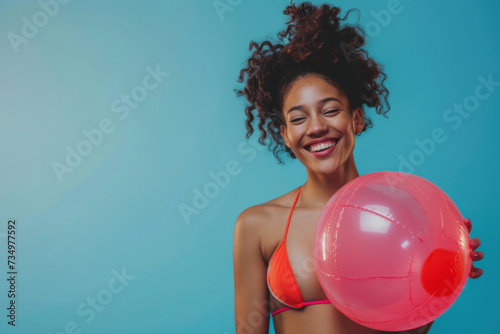Funny young happy African American woman in swimsuit having fun holding inflatable ball and going on summer holiday trip standing on blue studio background. Vacation tour and travel concept. © AI_images