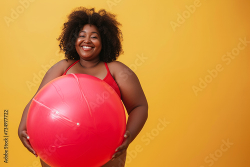 Funny young happy fat African American woman in red swimsuit having fun holding inflatable ball and going on summer holiday trip standing on yellow studio background. Vacation tour and travel concept © AI_images