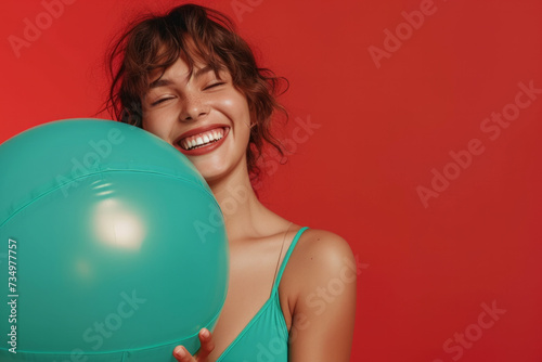 Funny young happy Latin woman in green swimsuit having fun holding inflatable ball and going on summer holiday trip standing on red studio background. Vacation tour and travel concept. © AI_images