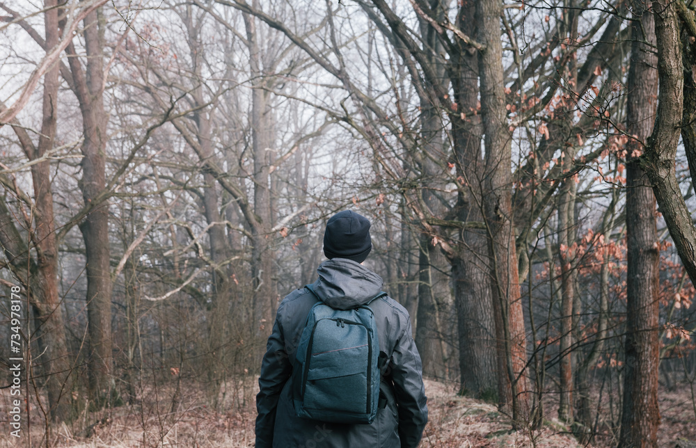 Man in cap and jacket walking through fog forest with backpack. Nature, travel background