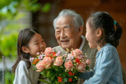Happy Japanese grandfather receives birthday presents from his loving family. Children together with grandmother give grandpa a card and a bouquet of beautiful flowers