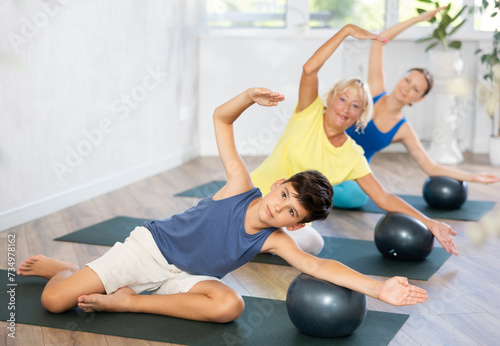 Family grandmother, mother and teen grandson perform fitness exercises sitting