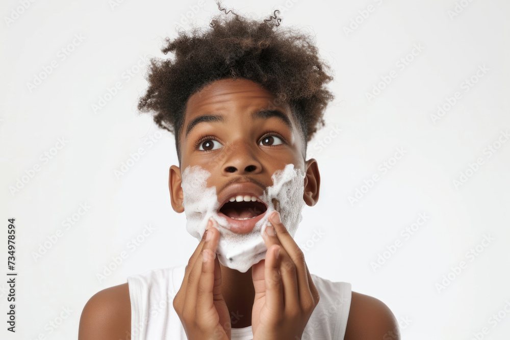 Handsome nervous African American teenage boy with foam on face learning to shave isolated on white studio background